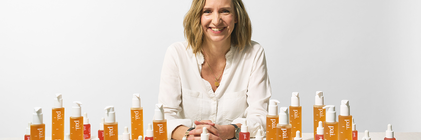 Person smiling at a table filled with Pai Skincare products, arranged in neat rows against a plain white background.