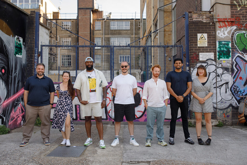 A group of seven LeftBrain team members standing together in an urban setting with graffiti-covered walls and industrial buildings in the background, smiling at the camera.